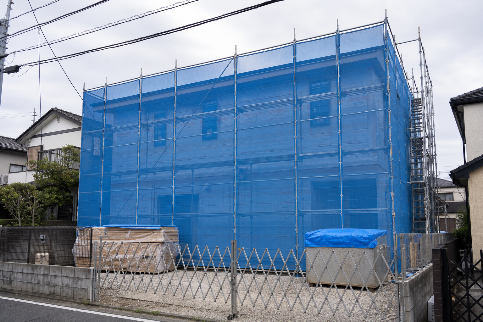 足場と青い養生シートで覆われた建築中の戸建て住宅
