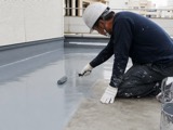 屋上の防水層をローラーで施工する職人